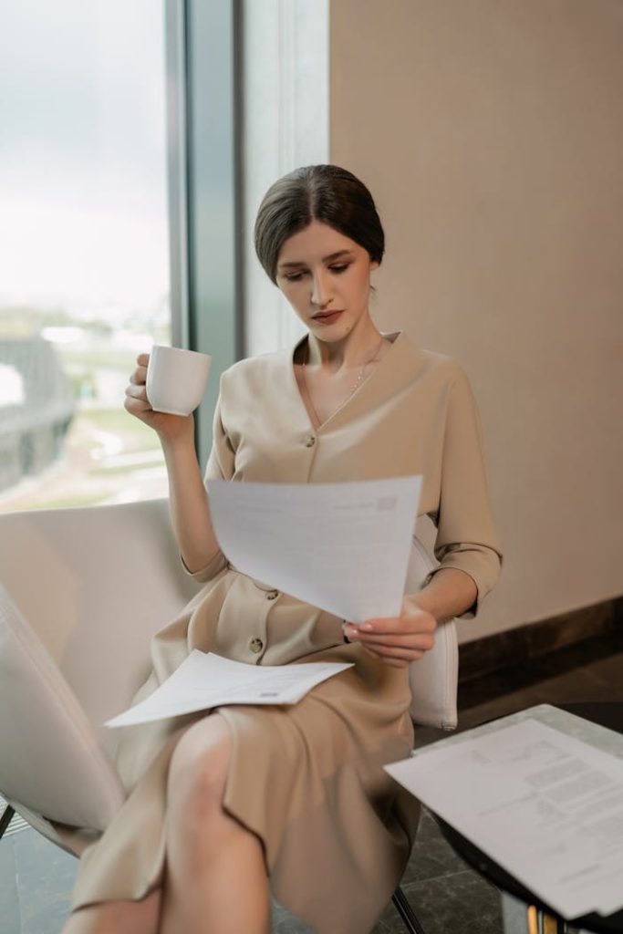 Businesswoman in an office setting reviewing documents while enjoying her coffee.